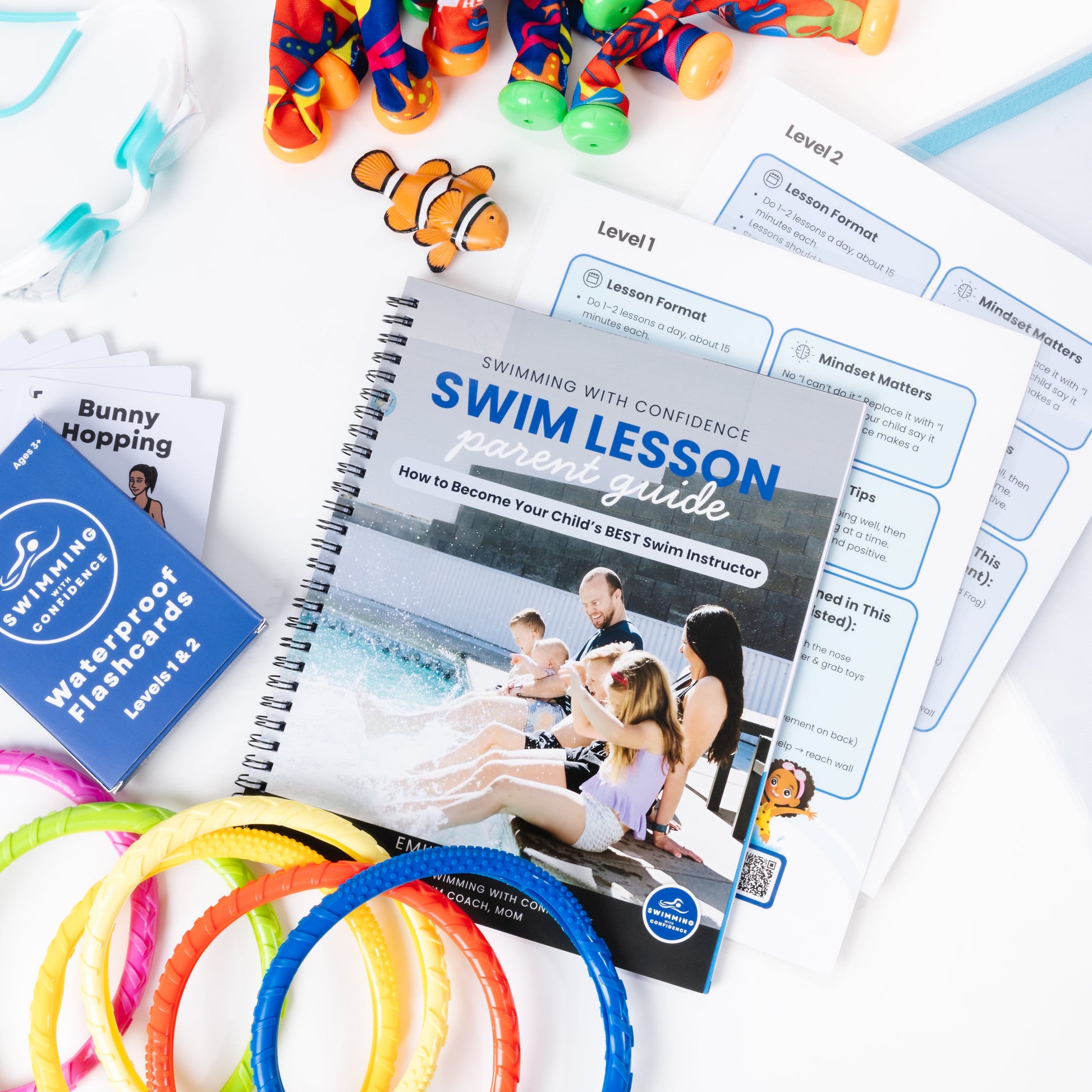 Swimming lesson materials including a workbook, goggles, and swim rings on a white surface.