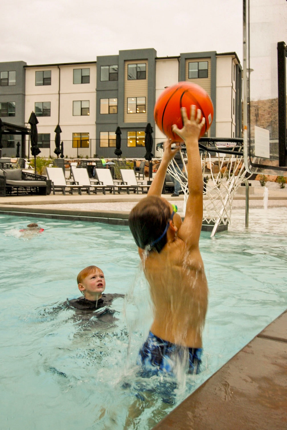 kids playing basketball in the pool a girl in the background swimming underwater